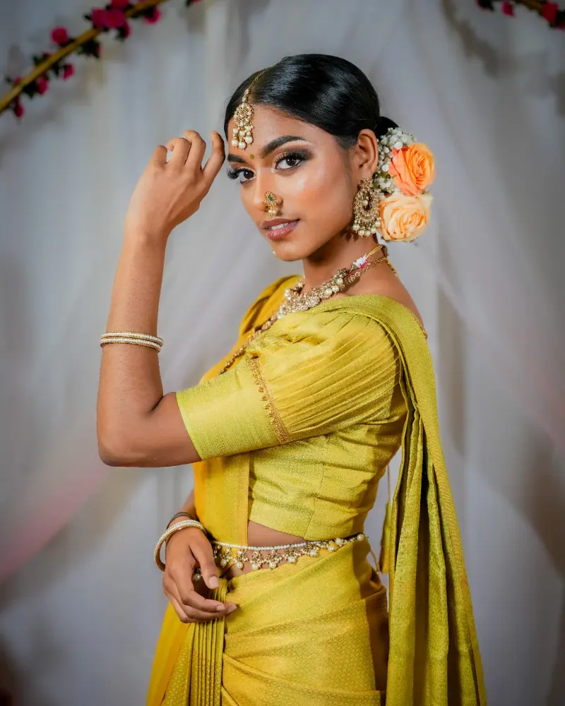 Modèle en saree jaune vert, bijoux dorés, chignon orné de roses orangées, main levée vers le visage.