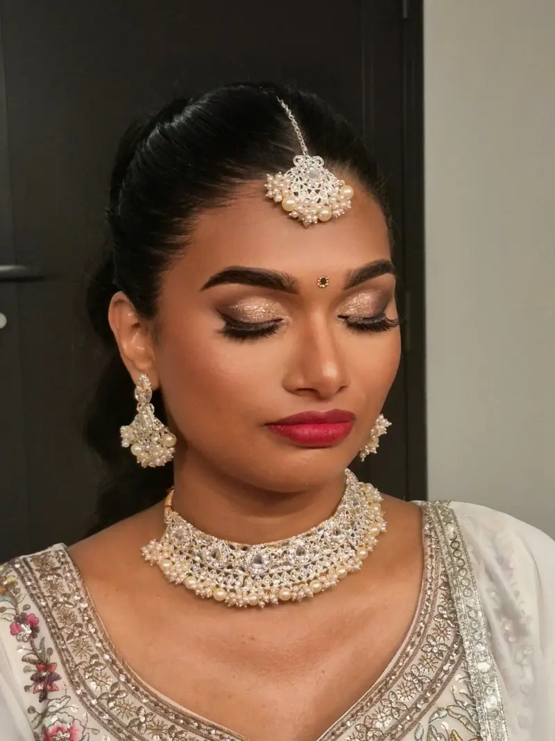 Portrait de Subasini, maquillage aux yeux dorés et lèvres rouges, maang tikka et parure de perles, chignon lisse.