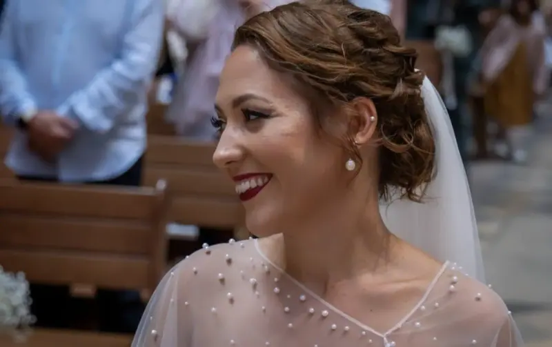 Clémence souriante dans une église, chignon souple et cape de tulle perlée.