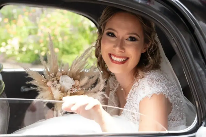 Amandine souriante à la fenêtre d'une voiture ancienne, bouquet de fleurs séchées.